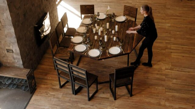 Woman waitress lights candles on table in modern restaurant with wooden interior, top view. Preparing the cafe for visitors. Event, party, restaurant business, festive table setting for holiday.
