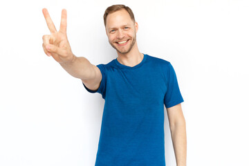 Happy White man showing peace gesture at camera. Portrait of smiling guy looking at camera and standing on white background. Satisfaction, achievement, winning concept