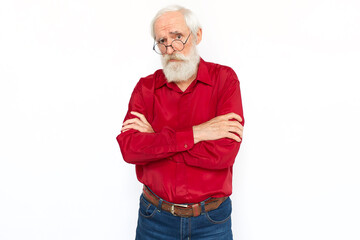 Confused senior man crossing arms. Ironic Caucasian male model with gray hair and beard in red shirt and glasses looking at camera, raising eyebrow, expressing doubt. Confusion concept