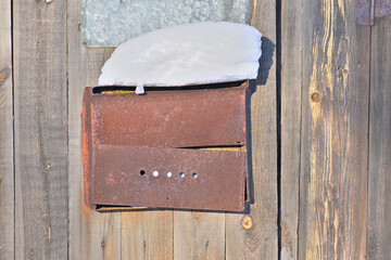 An old rusty mailbox on a wooden door on a winter day