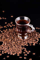 glass cup hot real brazilian arabica coffee roasted beans spilled and scattered on black background portrait, close-up vertical viewed from angle
