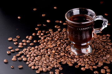 glass cup organic coffee straight from the producer hot brazilian arabica roasted beans spilled and scattered on a black background portrait, vertical close-up viewed from the front - obrazy, fototapety, plakaty