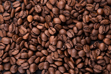 portion background of organic coffee beans direct from the Brazilian producer roasted arabica type spilled and scattered on a black background portrait texture - obrazy, fototapety, plakaty