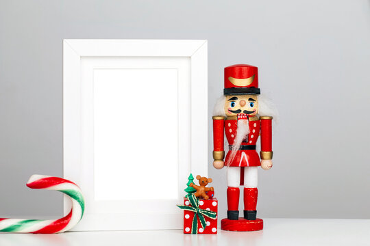 Christmas decoration with an old red nutcracker toy, lollipop cane and gift box on the table with white wooden frame - mockup for picture or photo