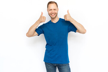 White man showing thumbs up while standing on white background. Happy bearded man in T-shirt looking at camera and showing approving gestures. Agreement, approval concept
