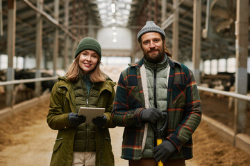 Fototapeta premium Portrait of young couple of farmers smiling at camera, working together with cattle on farm