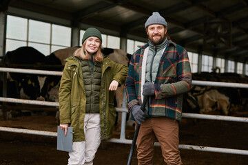 Portrait of young farmers or owners smiling at camera standing in cowshed