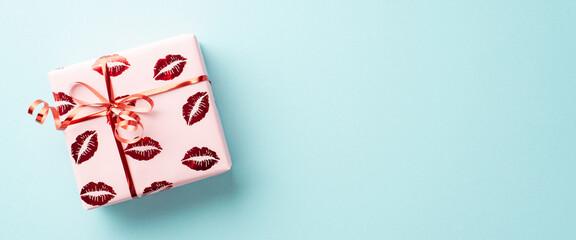 Valentine's Day concept. Top view photo of present box in wrapping paper with kiss lips pattern on isolated pastel blue background with copyspace