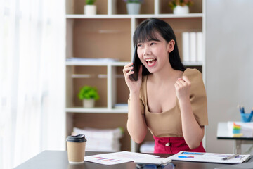 Beautiful Asian businesswoman using smartphone is delighted and excited by the success she has achieved through her office cell phone.