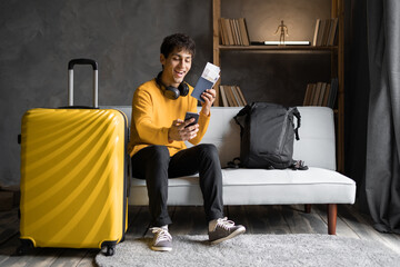Young man blogger with yellow suitcase taking selfie, getting ready for vacation at home. Happy male traveler making mobile photo of herself, traveling abroad