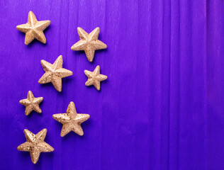 Fototapeta na wymiar Postcard with big and small golden decorative stars on violet paper textured background. Top view. Christmas, New Year holidays concept. Place for text.