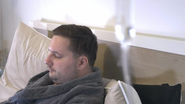 caucasian male patient sitting in bed room hospital clinic with IV drip Dextrose sterile solution blurred in foreground