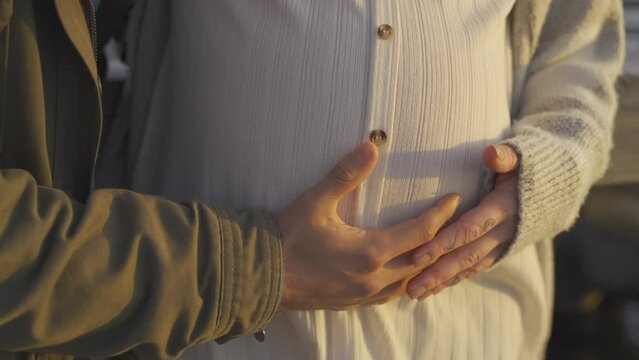 Close up of couple touching pregnant woman's belly on pier