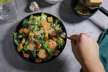 close up of woman eating Cesar salad with fork on grey marble table