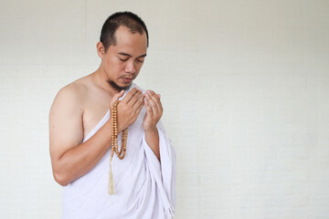 Asian muslim man wearing white ihram clothes and praying while holding prayer beads