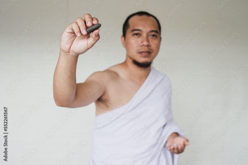 Wall mural asian muslim man performing the jamarat ritual (stoning the devil) during hajj season