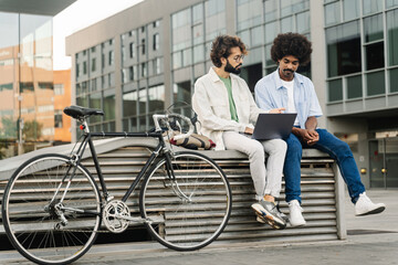 Fototapeta na wymiar Two young male freelancer friends working together on laptop - Modern coworkers sitting outdoors office with bicycle 