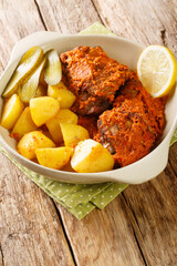 Galinha a Africana African Chicken from Macau served with potatoes, lemon and pickled cloiseup on the pot on the table. Vertical