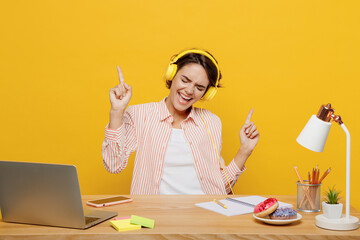 Young joyful fun employee business woman wear casual shirt headphones listen music sit work at...