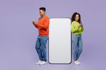 Full body fun young couple two friends family man woman wear casual clothes together big huge blank screen mobile cell phone with area use smartphone isolated on pastel plain light purple background.