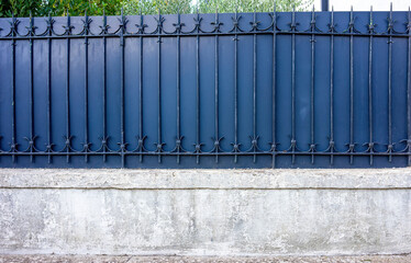 Frontal view of a blue metal fence on a gray wall. Ornate fence to a garden or backyard.