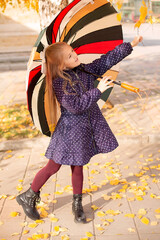 Naklejka premium a blonde girl in a blue polka dot jacket is standing on the street with a multicolored umbrella in her hands