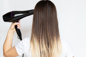 Fototapeta premium The girl dries her hair with a hairdryer on a white background, hair dryer and hair, hairdresser