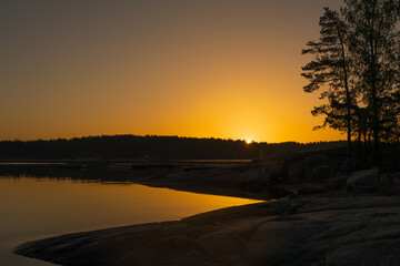 A golden-orange sunset on the sea with a silhouette of a tree line on the horizon. Nature of Finland. Scandinavia. Natural background. Space for text.