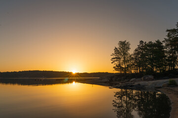Fototapeta premium A golden-orange sunset on the sea with a silhouette of a tree line on the horizon. Nature of Finland. Scandinavia. Natural background. Space for text.