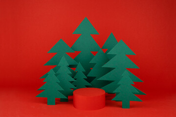 Bright red New Year background with red cylinder podium mockup, green paper spruces as forest in...