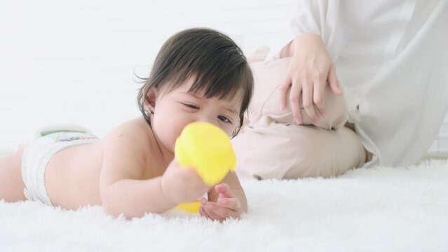 Baby girl lying on the floor holding a rubber duck toy to chew and itchy gums with mom.