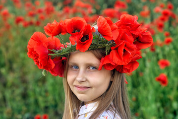 Portrait of a beautiful young girl in a wreath of red poppies in nature