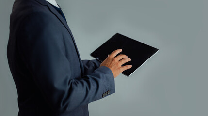 Asian businessman in suit touching tablet blank screen gray background.