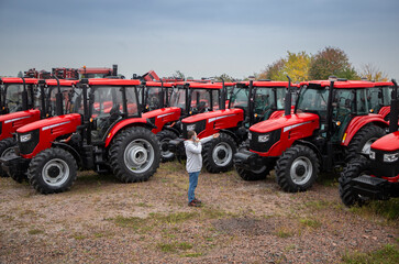 Presentation and sale of new red tractors standing in a row. A man speaks on the phone and points to one of the agricultural tractors. Equipment for agriculture, agribusiness and farming