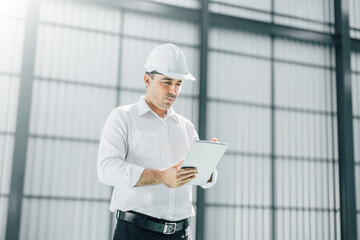 warehouse manager with tablet and ..radio communication his worker working in background in...