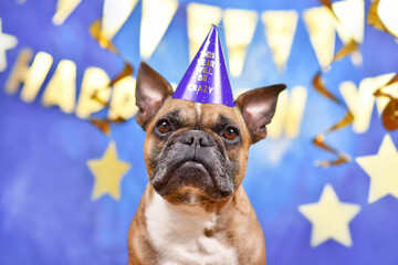French Bulldog dog wearing New Year's Eve party celebration hat in front of blue background...