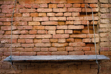 An empty, old wooden board hangs on two ropes in front of a red brick wall. Well suited for product presentation with copy space.