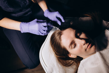 Obraz na płótnie Canvas cropped female person at trichologist office get injections in head skin by professional doctor's hands holding disposable syringe under patient's head. Porcedure against hair loss and for skin health