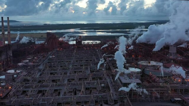 Drone shot orbiting coal and metal factory at dawn, large steam smoke stacks operating. Queensland Australia 4K