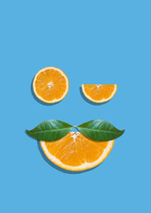 Creative summer face with eyes made of orange fruit slices and mustache made of leaves on bright blue vibrant background. Orange juice minimal tropic concept. Winking eye funny idea - 552278364