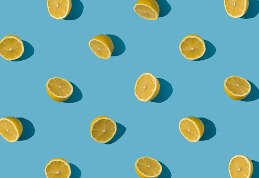 Summer pattern made with fresh yellow lemon halfs on bright light blue background. Minimal background summer concept on bright sunlight with sharp shadows