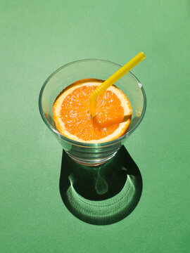 Orange juice with yellow straw in a glass concept on green background. Tropical summer minimal concept sunlit with sharp shadows