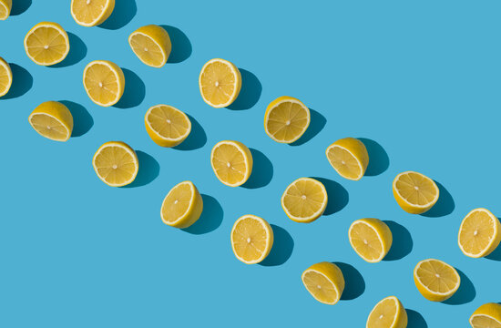 Diagonal summer pattern for banners made with fresh yellow lemon halves on bright blue pastel background. Minimal background summer concept on bright sunlight with sharp shadows