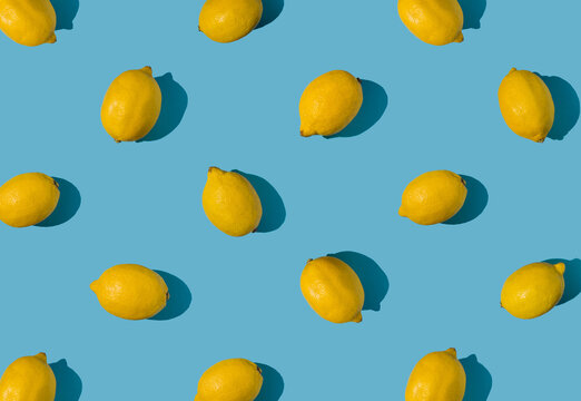 Summer pattern made with fresh yellow whole lemons on vibrant light blue background. Minimal background summer concept on bright sunlight with sharp shadows