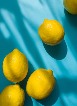 Composition with whole ripe yellow lemons on bright blue background. Summer time flat lay with daylight and sharp shadows. Top view
