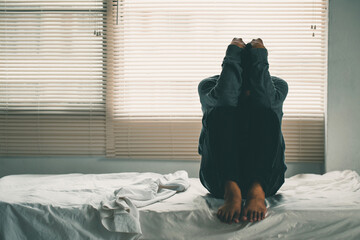 Depressed man losing his job and heartbroken sitting alone in bed near a window in dark with the low light environment, PTSD Mental health, and depression concept.psychological problem, sadness. - obrazy, fototapety, plakaty
