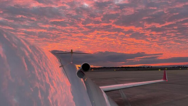 Extraordinary red sky reflected on the upper fuselage of a jet just before sunset, unfocused-focused view, with a follow me car at the back. Natural colors.