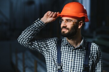 Portrait of Professional Heavy Industry Engineer Worker Wearing Safety Uniform, Hard Hat Smiling. In the Background Unfocused Large Industrial Factory.