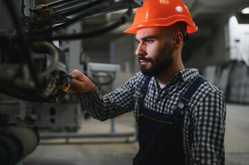 Portrait of Professional Heavy Industry Engineer Worker Wearing Safety Uniform, Hard Hat Smiling. In the Background Unfocused Large Industrial Factory.