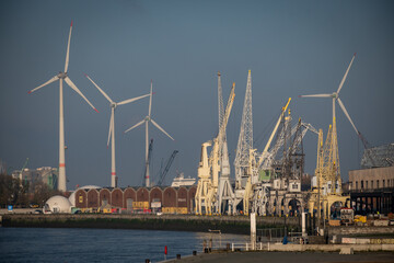 Fototapeta na wymiar The remaining industrial part of Antwerp with colleaction of cranes on the bank of the river scheldt with wind turbines in the background